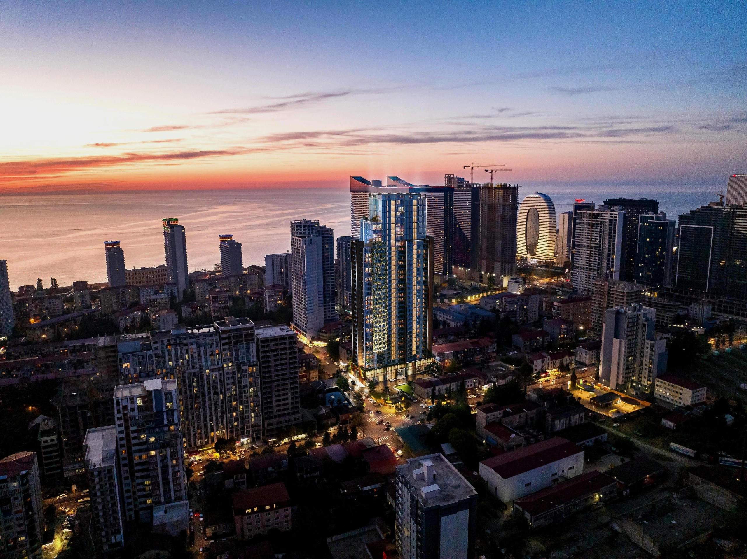 Архитектурная 3D-визуализация современного высотного жилого комплекса, интегрированная в вечернюю панораму прибрежного города.